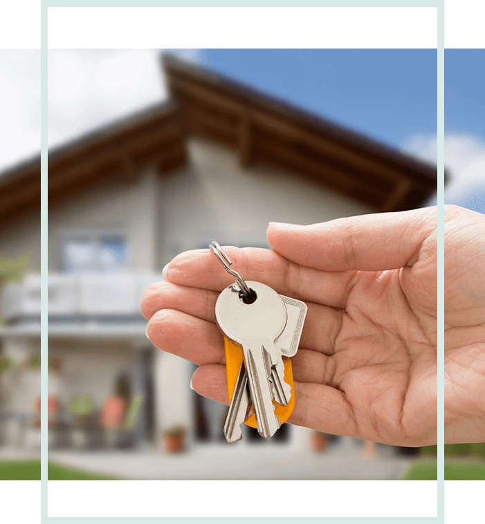 A hand holding keys in front of a house.